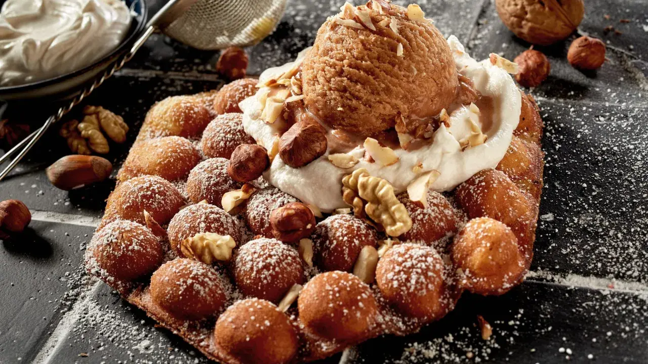 Bubble Eis auf einem Waffel-Snack, bestreut mit Puderzucker und garniert mit Nüssen und einer Kugel Eis.