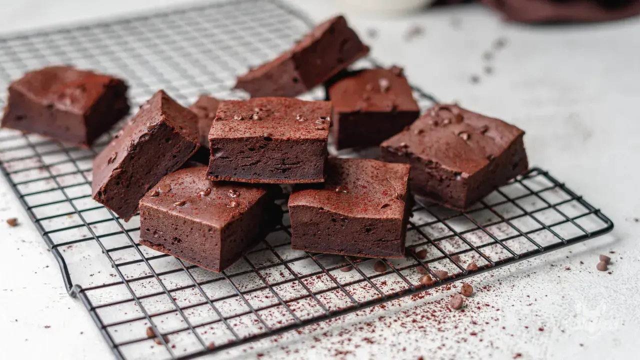 Saftige low carb brownies, bestreut mit Kakaopulver und Schokostückchen, auf einem Kuchengitter.