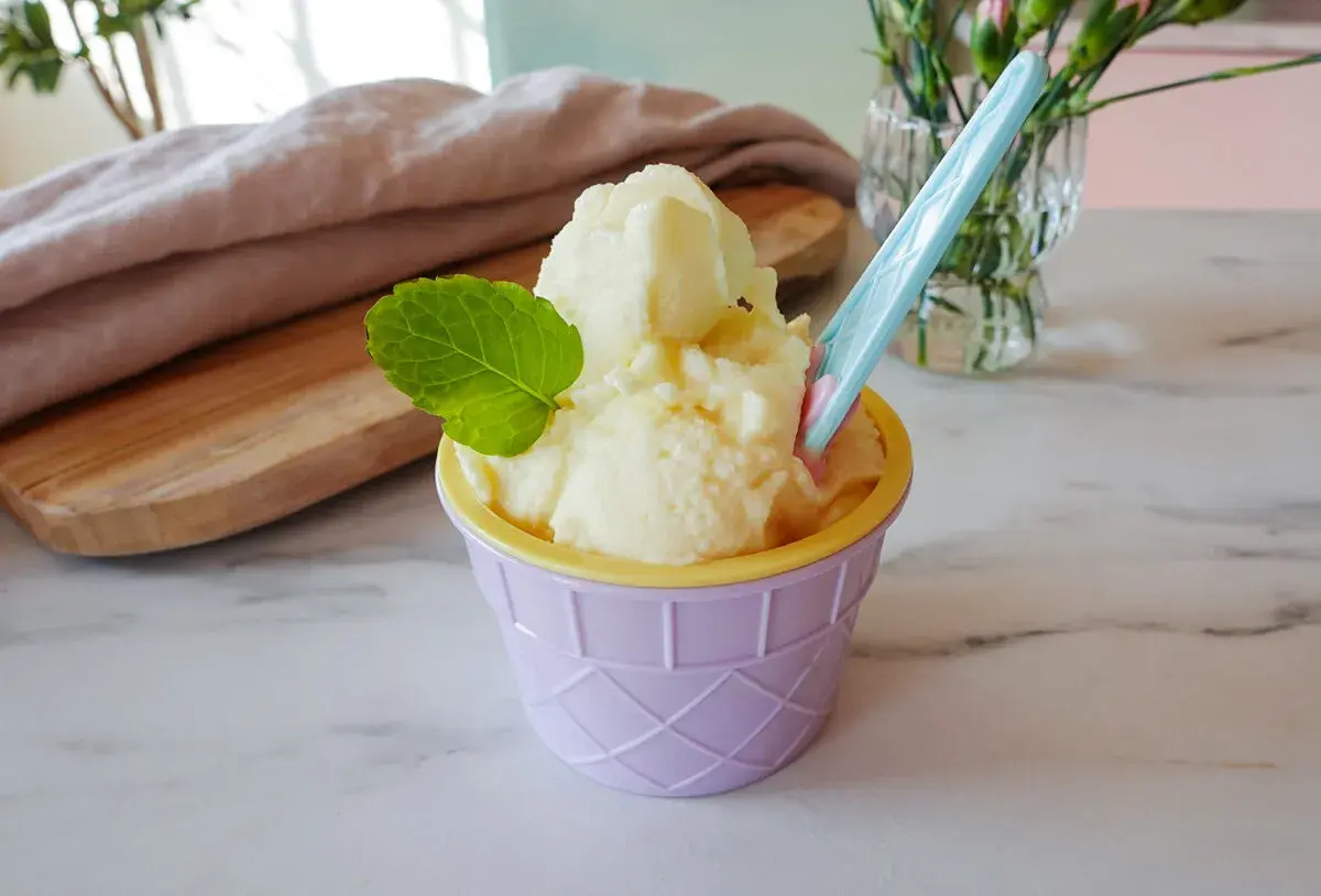 Ein cremiges Ananas Eis in einem lila Becher, garniert mit Minze. Perfekt für heiße Tage!