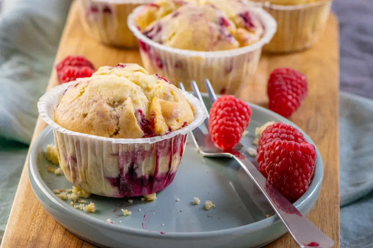 Saftige Himbeer Muffins auf einem Teller, garniert mit frischen Himbeeren. Ein Genuss für jeden Kaffeetisch.