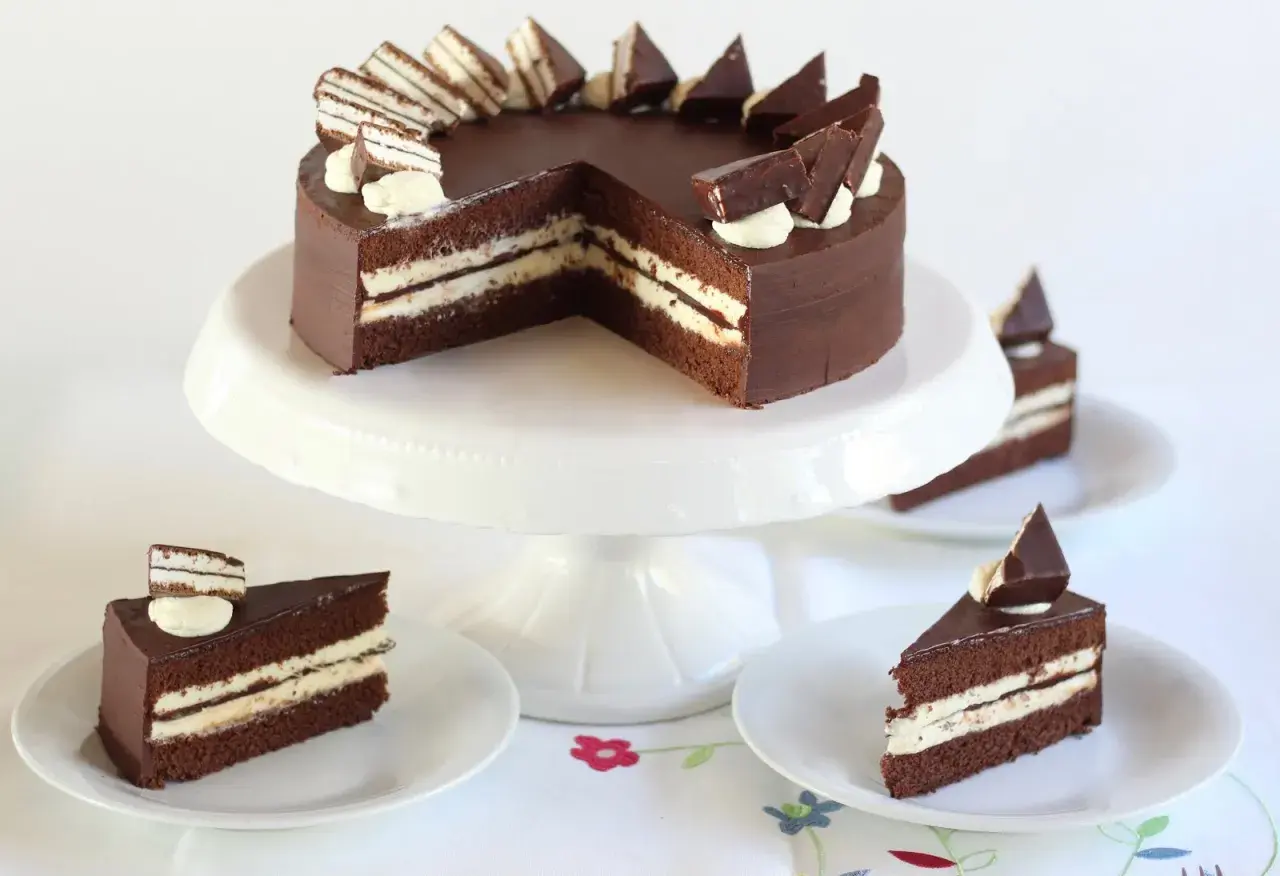 Schokoladentorte mit cremiger Füllung und Schokostückchen, inspiriert von der Kinder Pingui Torte. Serviert auf einem Tortenständer mit einzelnen Tortenstücken.