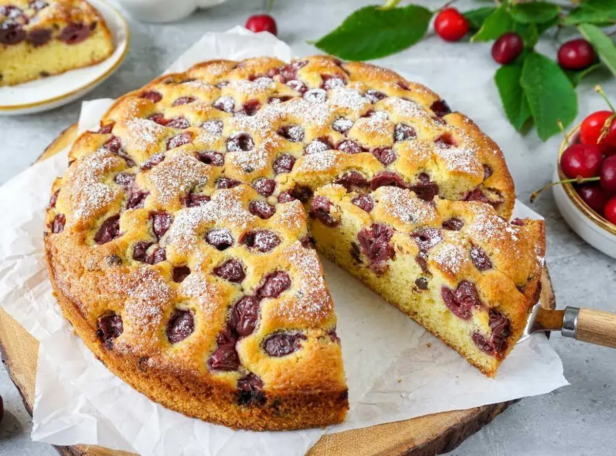 Saftiger Kuchen mit Kirschen, bestäubt mit Puderzucker. Ein Stück wurde bereits herausgeschnitten.