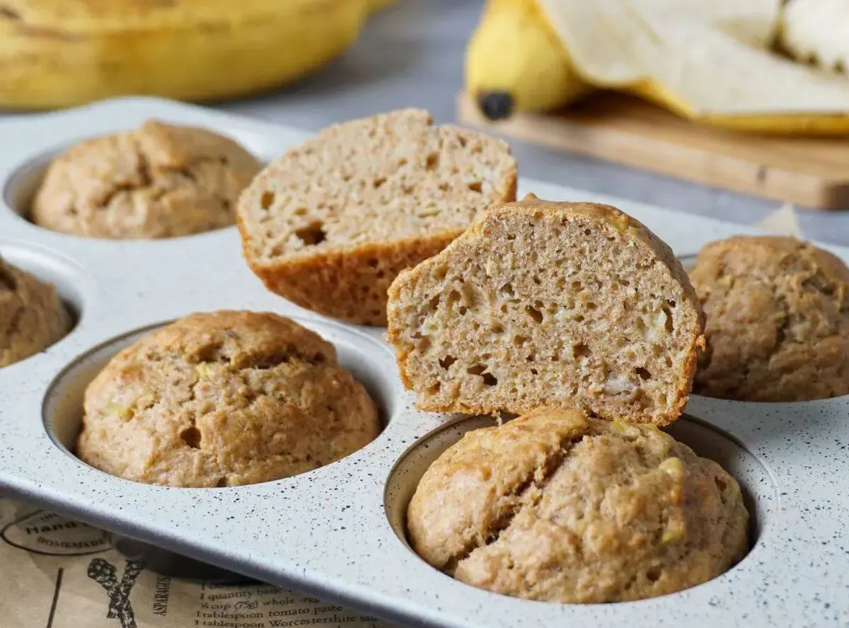 Saftige bananenmuffins ohne zucker, gebacken in einer Muffinform. Eine Hälfte ist aufgeschnitten und zeigt die lockere Krume.