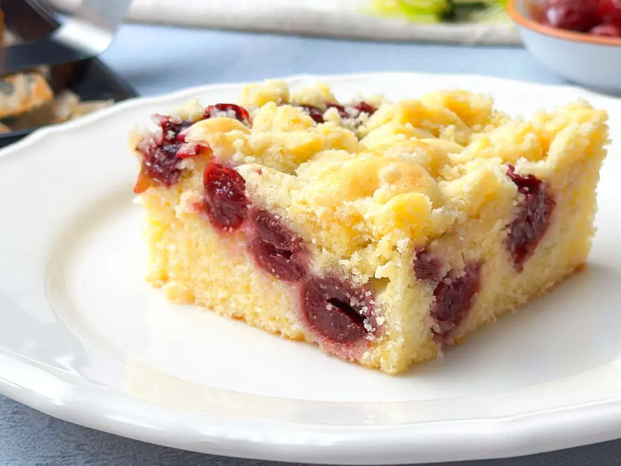 Ein saftiges Stück Kirsch-Streuselkuchen vom Blech, mit vielen Kirschen und knusprigen Streuseln, auf einem weißen Teller.