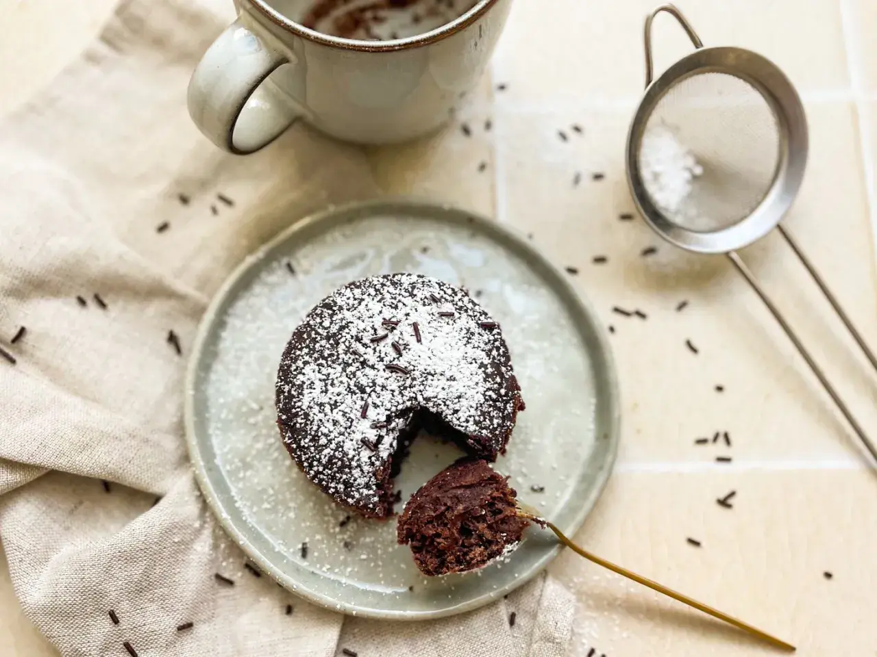 Ein saftiger Schoko-Tassenkuchen ohne Ei, bestäubt mit Puderzucker und Schokostreuseln, bereit zum Genießen.