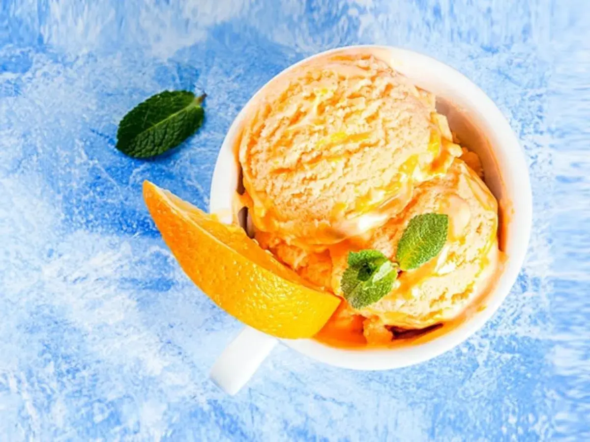 Erfrischendes orangen sorbet in einer Schale, garniert mit Minze und einer Orangenspalte auf blauem Untergrund.