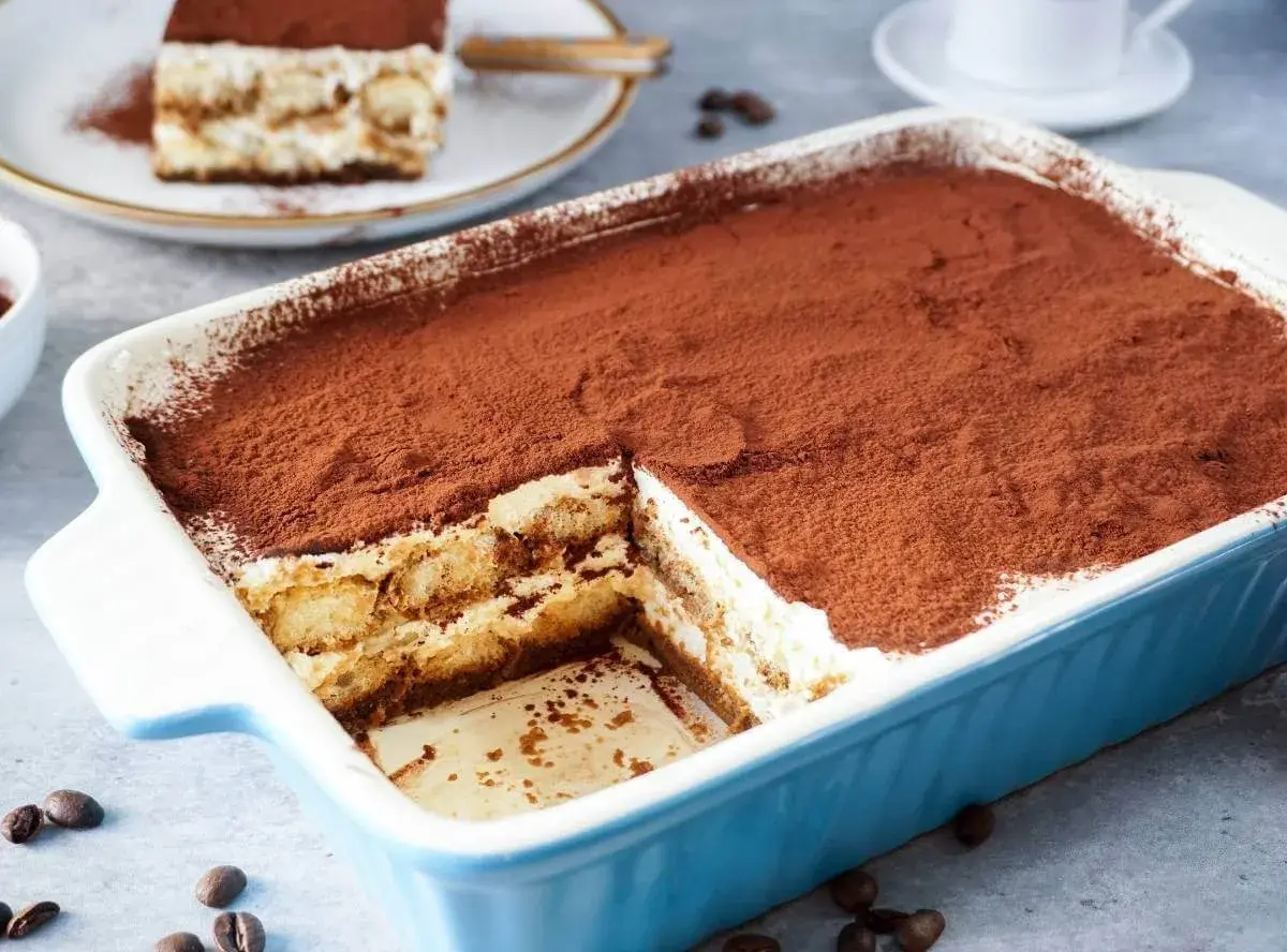 Ein cremiges Tiramisu, perfekt für ein tiramisu rezept ohne alkohol. Mit Kakaopulver bestäubt und in einer blauen Auflaufform serviert.
