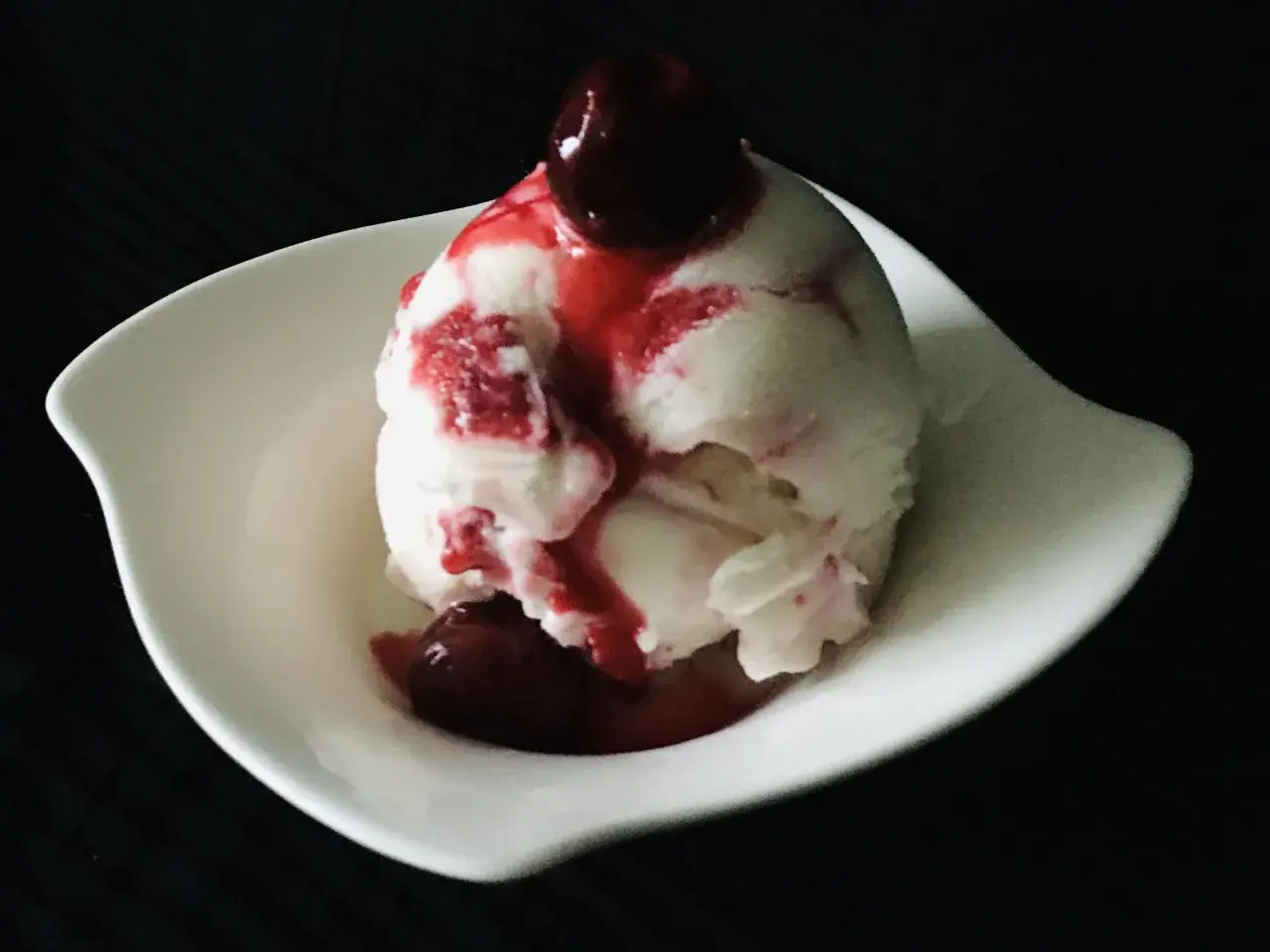 Ein Löffel cremiges Sauereis mit Kirschsauce und einer ganzen Kirsche obendrauf, serviert in einer weißen Schale.
