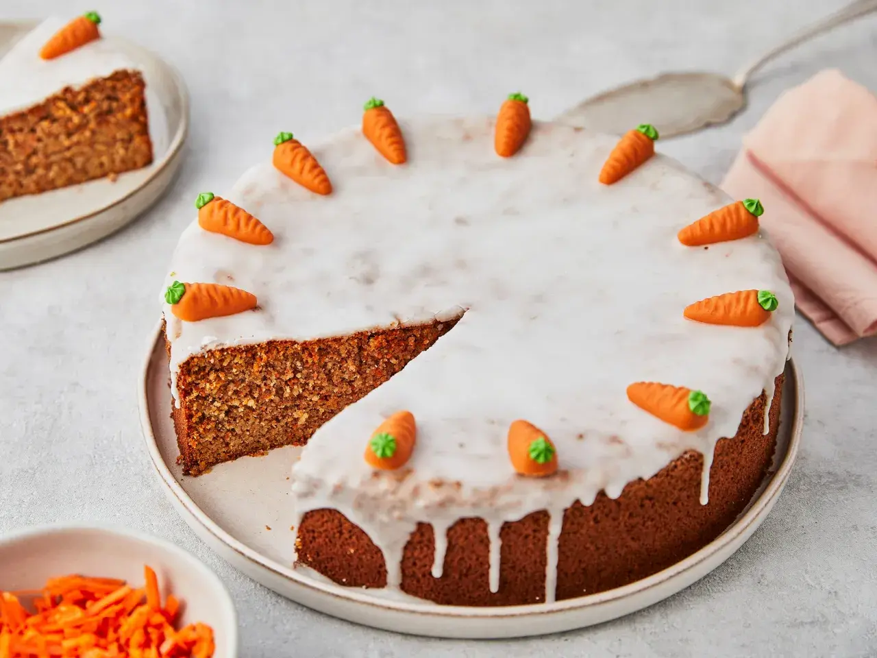 Ein saftiger karottenkuchen ohne mehl, verziert mit Zuckermöhren und Zuckerguss. Ein Stück ist bereits angeschnitten.