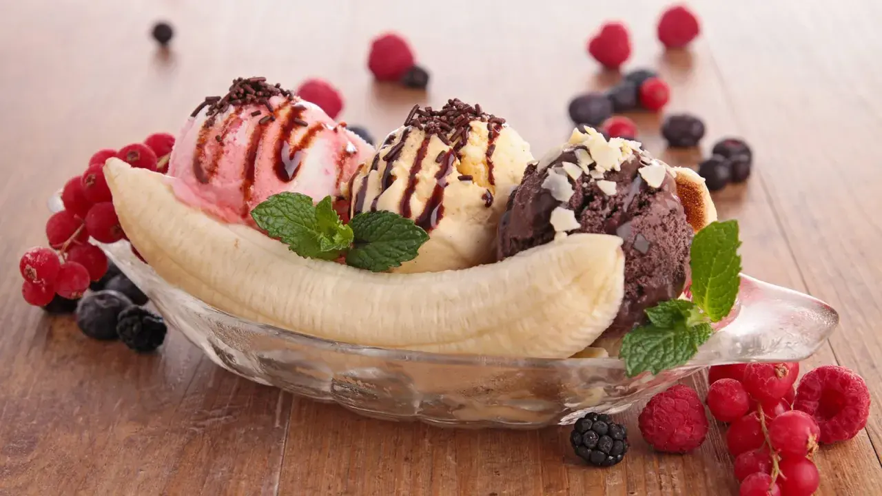 Ein köstlicher Bananensplit Eis mit drei Kugeln Eis, garniert mit Beeren und Minze.