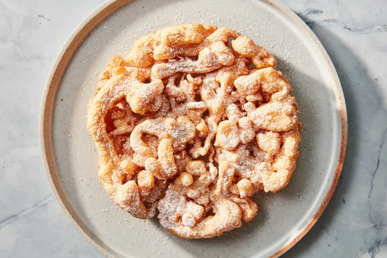 Ein goldbrauner, puderzuckerbestäubter **Funnel Cake** auf einem grauen Teller.
