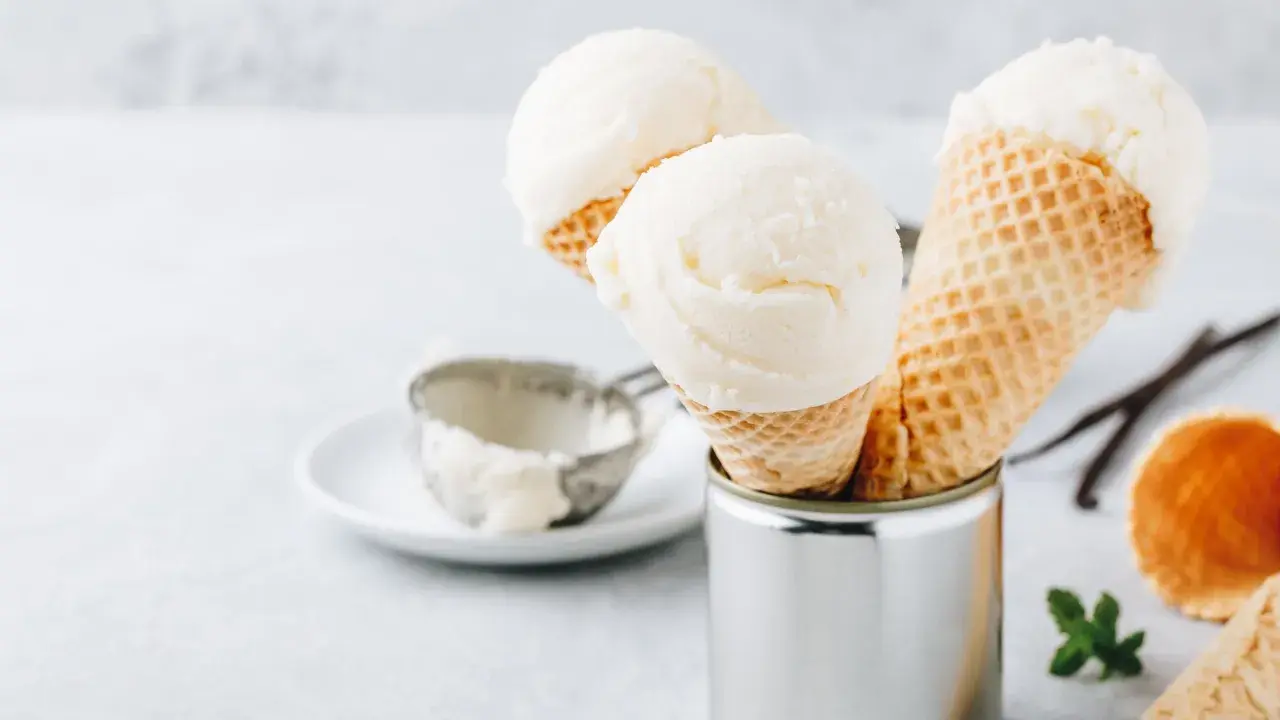 Cremiges griechischer joghurt eis ohne eismaschine in Waffelhörnchen. Ein Löffel und Vanilleschoten liegen daneben.
