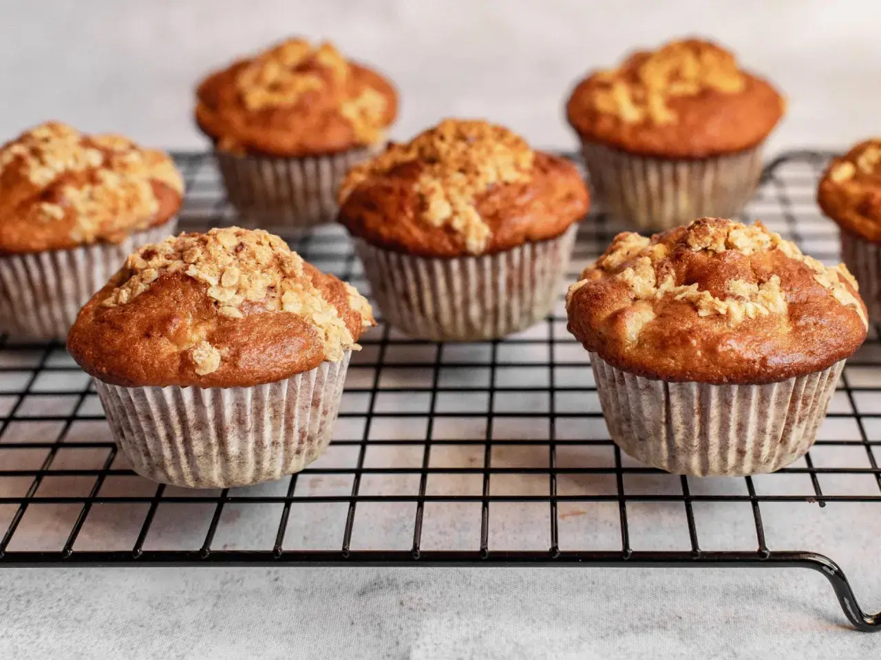 Mehrere goldbraune Haferflocken Muffins mit knuspriger Streusel-Decke auf einem Kuchengitter.