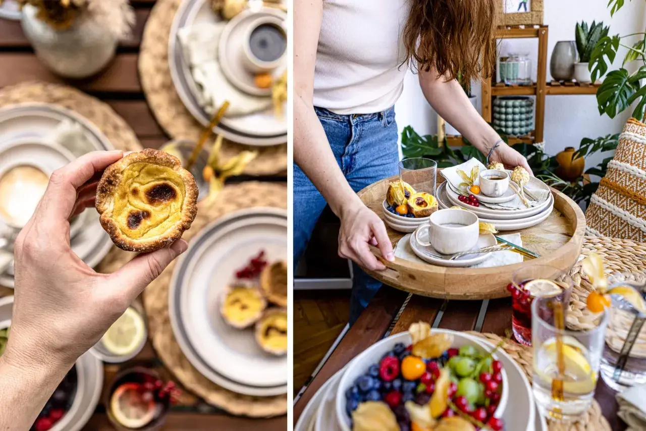 Hand hält ein knuspriges Pastel de Nata. Auf einem Tablett warten weitere Törtchen, Beeren und Kaffee.