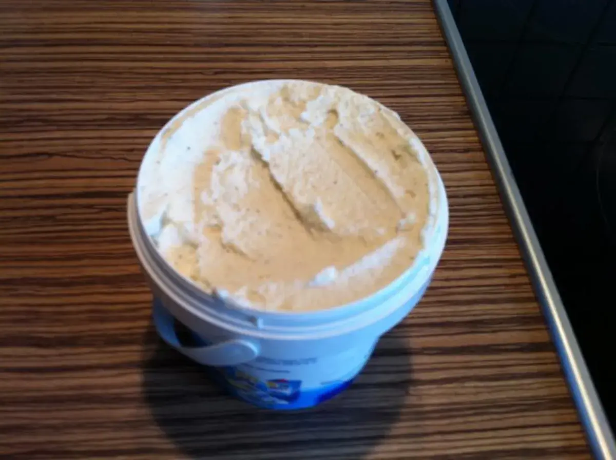 Ein Behälter mit cremigem, selbstgemachtem laktosefreiem Eis steht auf einer Holzoberfläche.