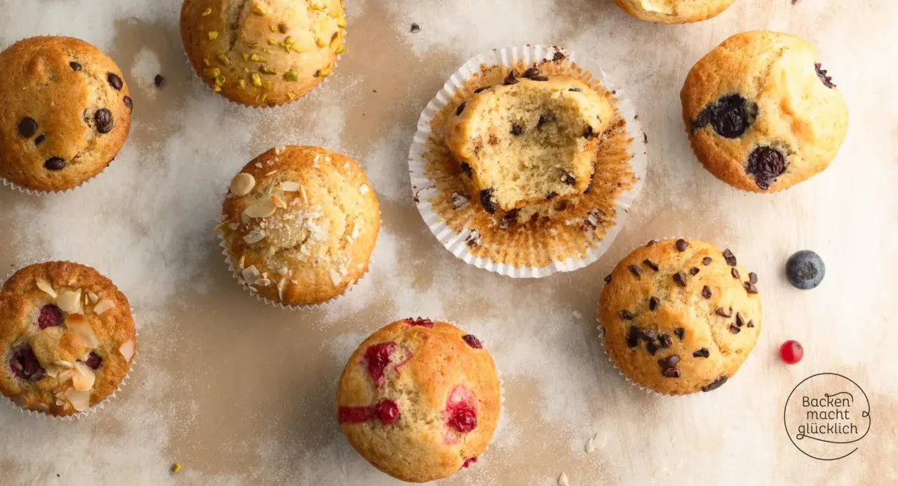 Verschiedene Muffins, die nach einem Muffins Grundrezept gebacken wurden: mit Schokostückchen, Blaubeeren, Himbeeren und Mandeln. Einer ist angeknabbert.