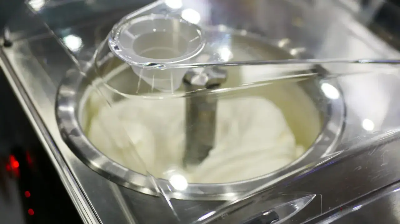 Cremiges Sahneeis wird in einer Eismaschine zubereitet. Der Rührarm dreht sich, um die perfekte Konsistenz zu erzeugen.