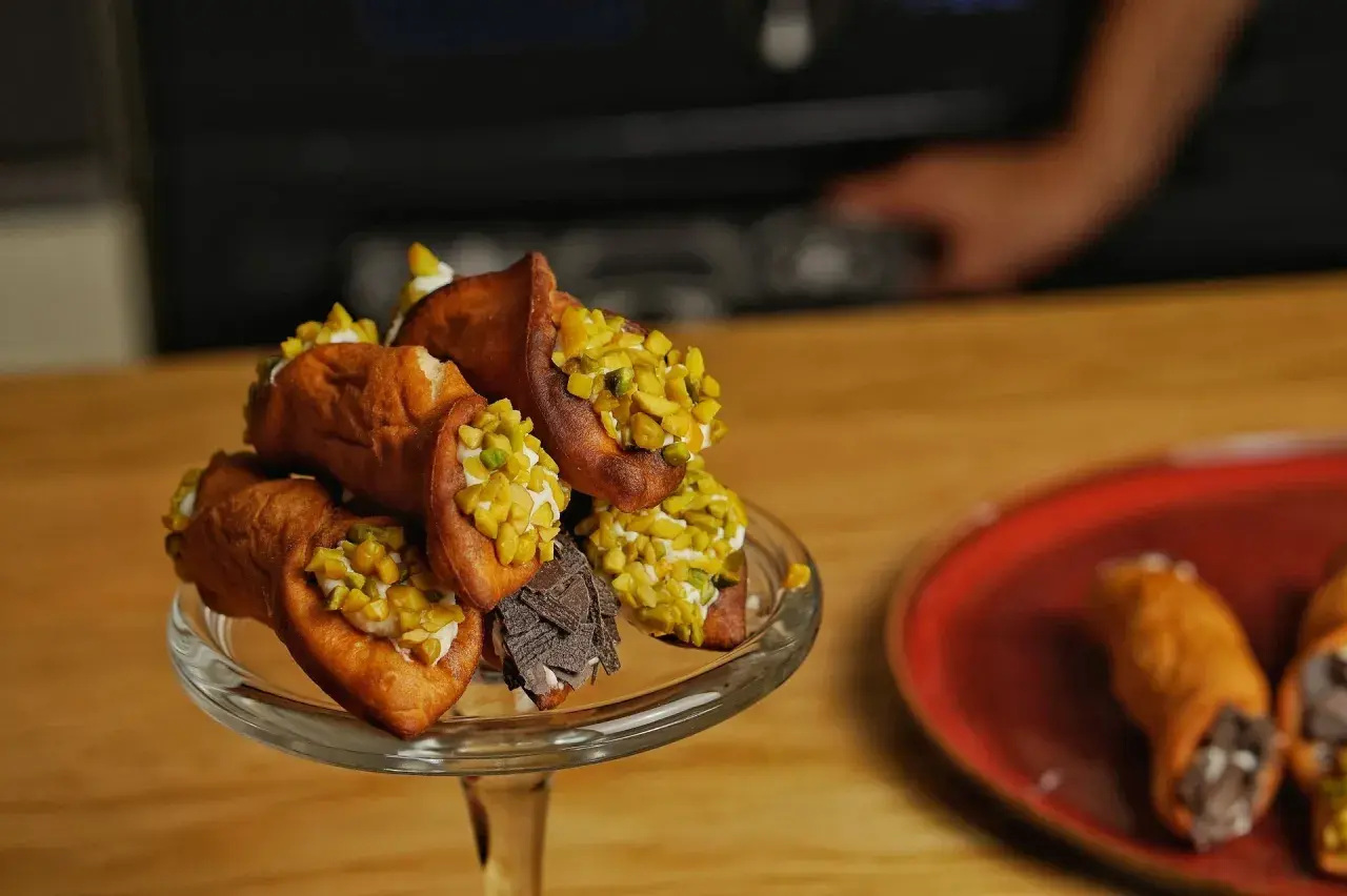 Ein Glasständer voller Cannoli, garniert mit Pistazien und Schokolade. Ein köstliches Cannoli-Rezept zum Nachmachen.