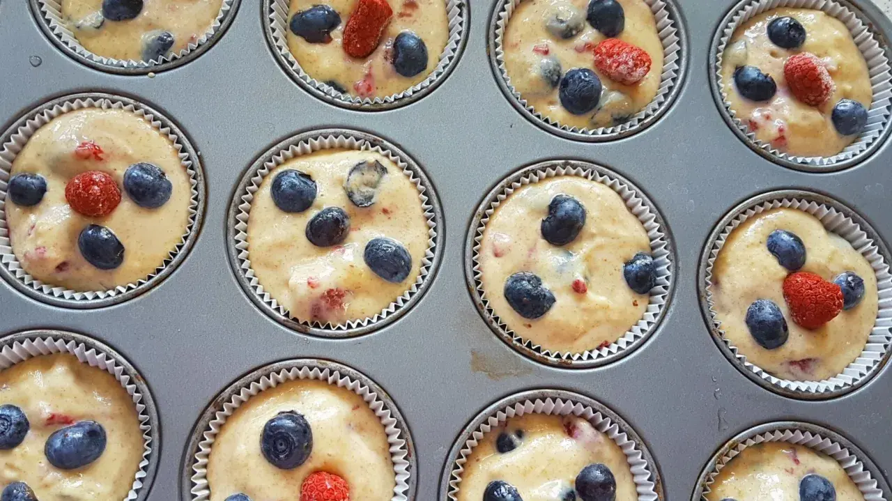 Frisch zubereiteter Teig für Heidelbeer Muffins, mit saftigen Blaubeeren und roten Beeren in einer Muffinform.