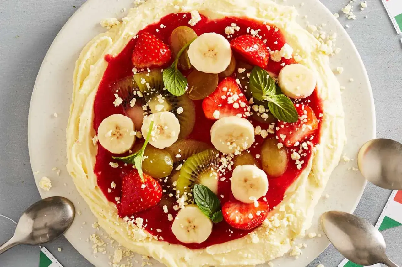 Fruchtige eis pizza mit Erdbeeren, Bananen, Kiwi und Trauben auf cremigem Boden, garniert mit Minze.