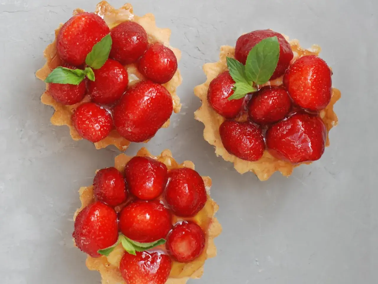 Drei köstliche Erdbeer Tartelettes, garniert mit frischer Minze, auf grauem Untergrund.