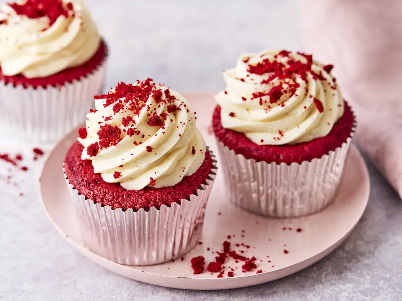 Zwei köstliche red velvet cupcakes mit cremiger Glasur und roten Krümeln, auf einem rosa Teller.