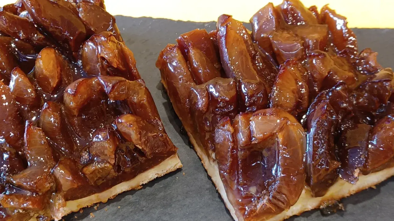 Zwei Stücke saftiger Zwetschgenkuchen vom Blech, glänzend und karamellisiert, auf dunkler Platte angerichtet.
