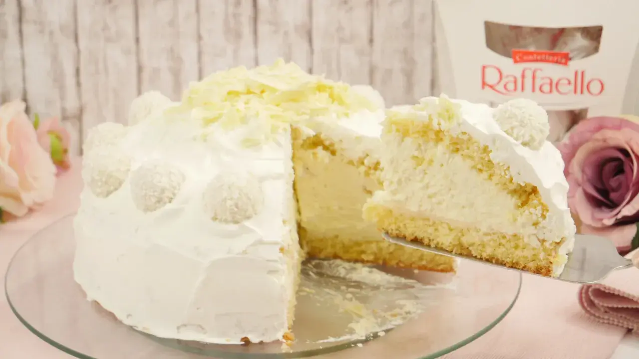 Eine köstliche Raffaello Torte, verziert mit Kokosraspeln und weißer Schokolade. Ein Stück wird gerade serviert.