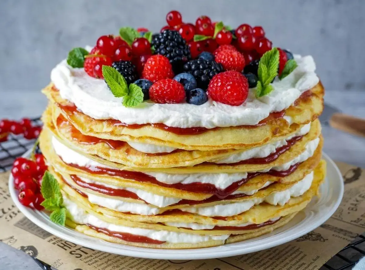 Eine hohe Pfannkuchen Torte mit Sahne und roter Marmelade, gekrönt mit frischen Beeren und Minze.