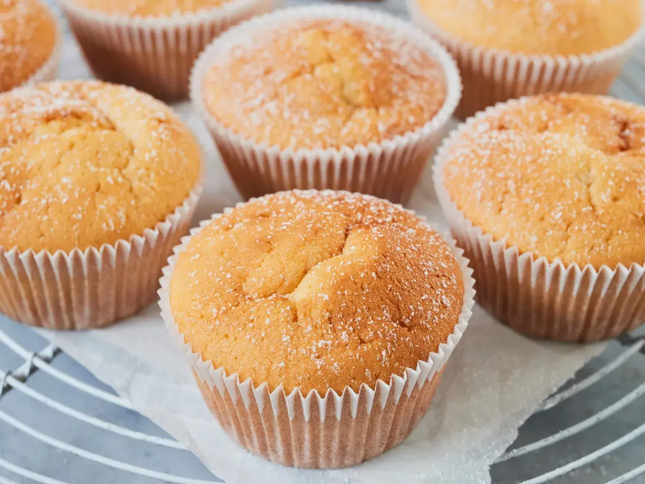 Frisch gebackene Quark Muffins, leicht mit Puderzucker bestäubt, auf einem Gitter.