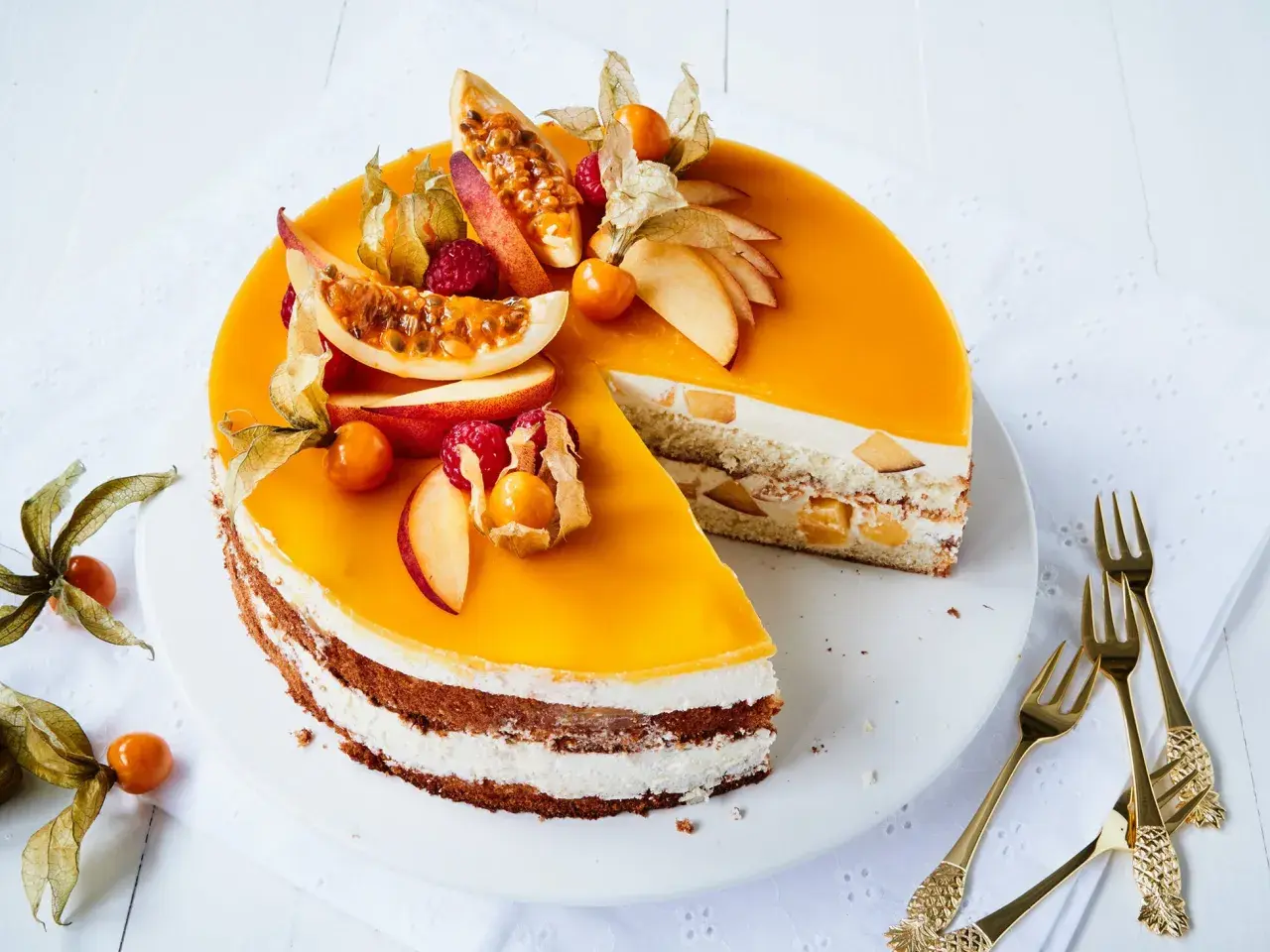 Eine köstliche Maracuja Torte mit frischen Früchten und Sahne. Ein Stück ist bereits angeschnitten, daneben liegen goldene Gabeln.