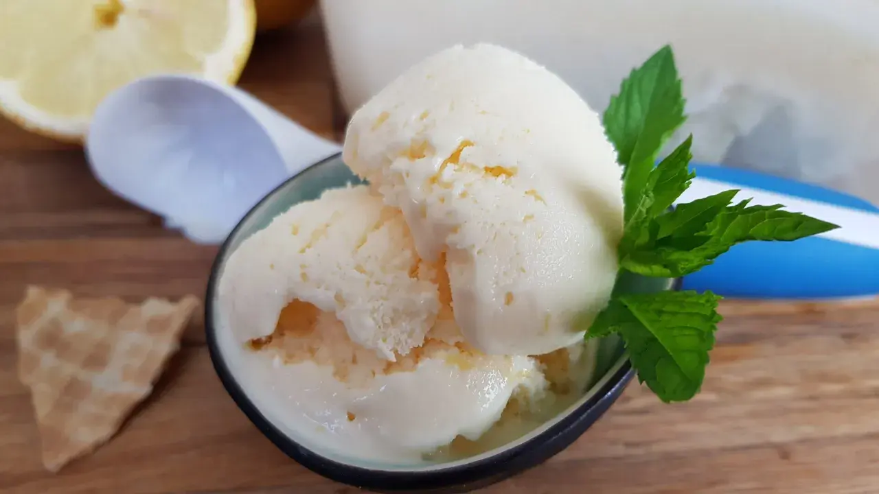 Erfrischendes zitroneneis mit joghurt, garniert mit Minze, daneben eine Waffel und Zitronenspalten.