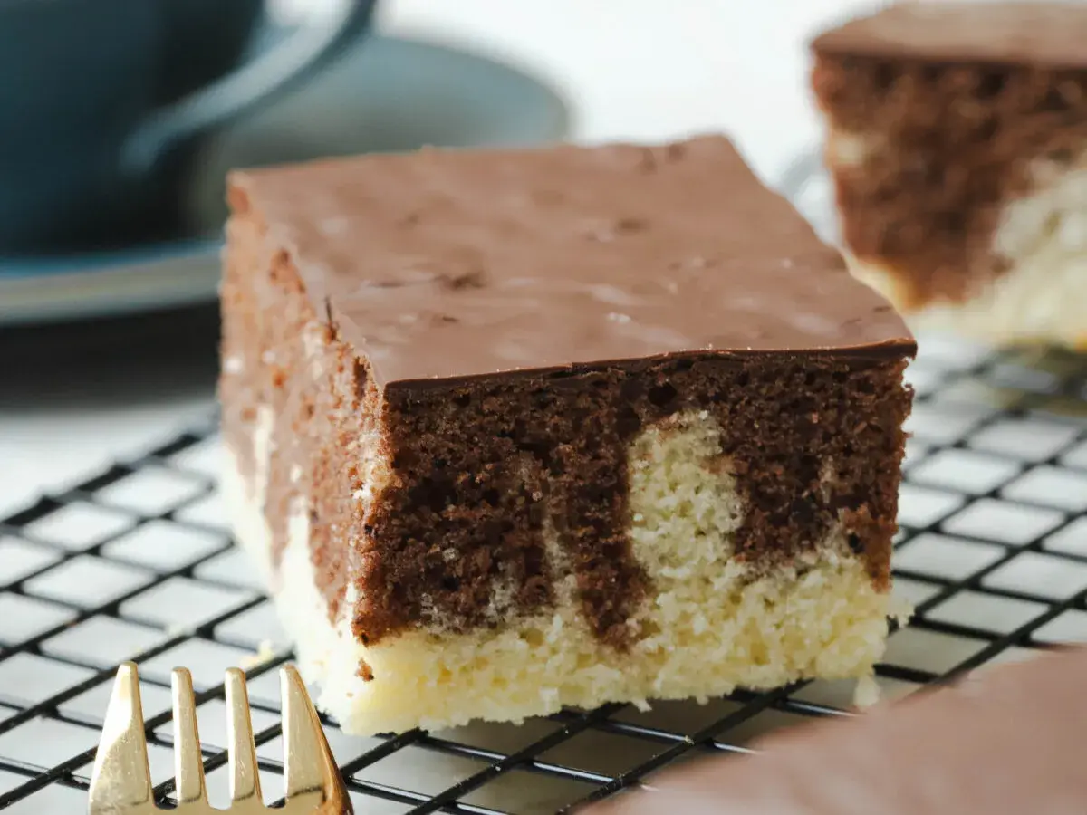 Ein Stück saftiger Marmorkuchen vom Blech mit Schokoladenglasur auf einem Kuchengitter.