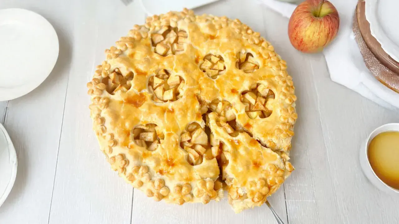 Goldbrauner Apfelkuchen mit Blätterteig-Dekor, ein Stück herausgeschnitten.