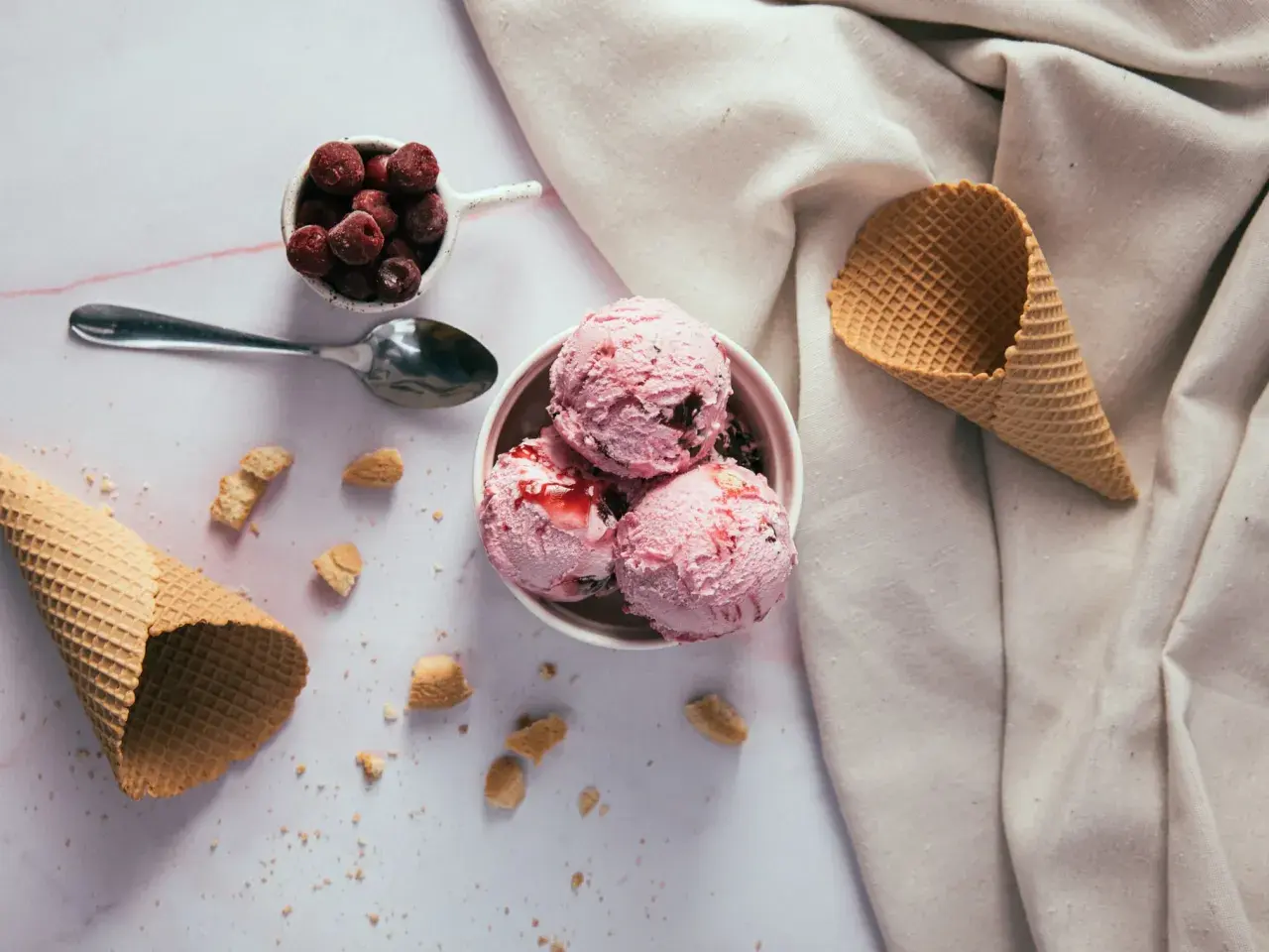 Schüssel mit rosa Eiskugeln, Kirschen und Waffelhörnchen. Ein süßer Genuss, der trotz der Kalorien verlockt.
