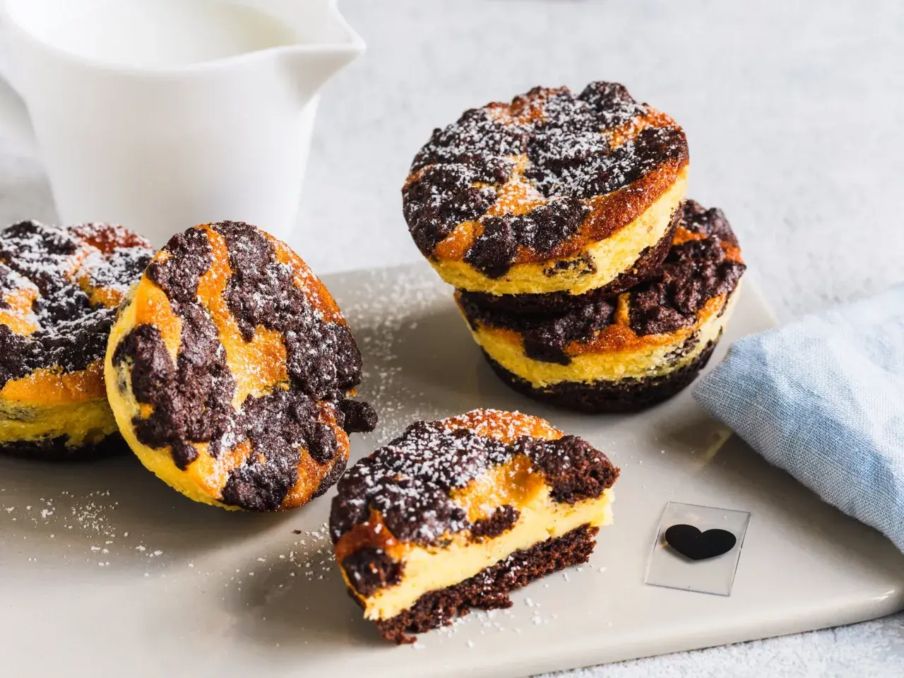 Leckere zupfkuchen muffins mit Puderzucker bestäubt, daneben ein Milchkännchen und ein blaues Tuch.