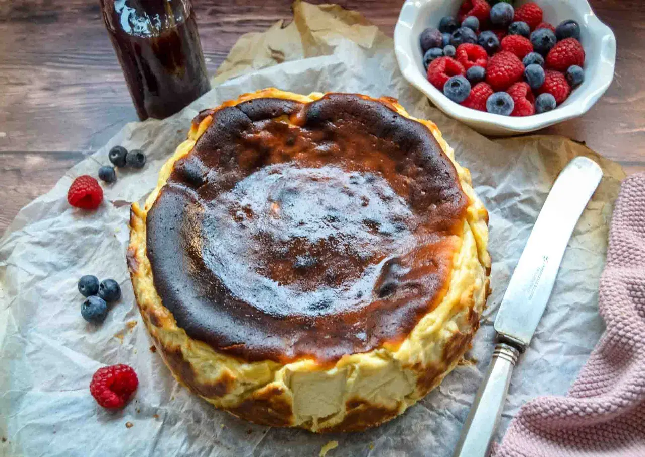 Ein perfekt gebackener San Sebastian Cheesecake mit karamellisierter Kruste, garniert mit frischen Beeren und einem Glas Marmelade.
