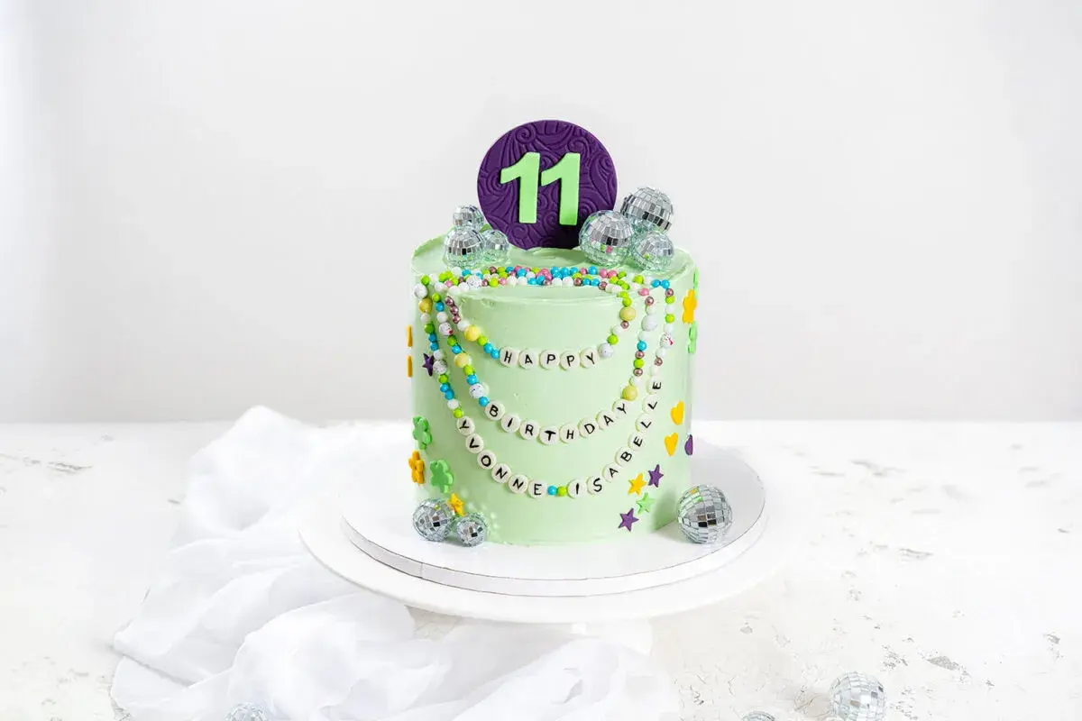 Eine bunte kinder torte für den 11. Geburtstag mit Perlenketten, Disco-Kugeln und Blumen.