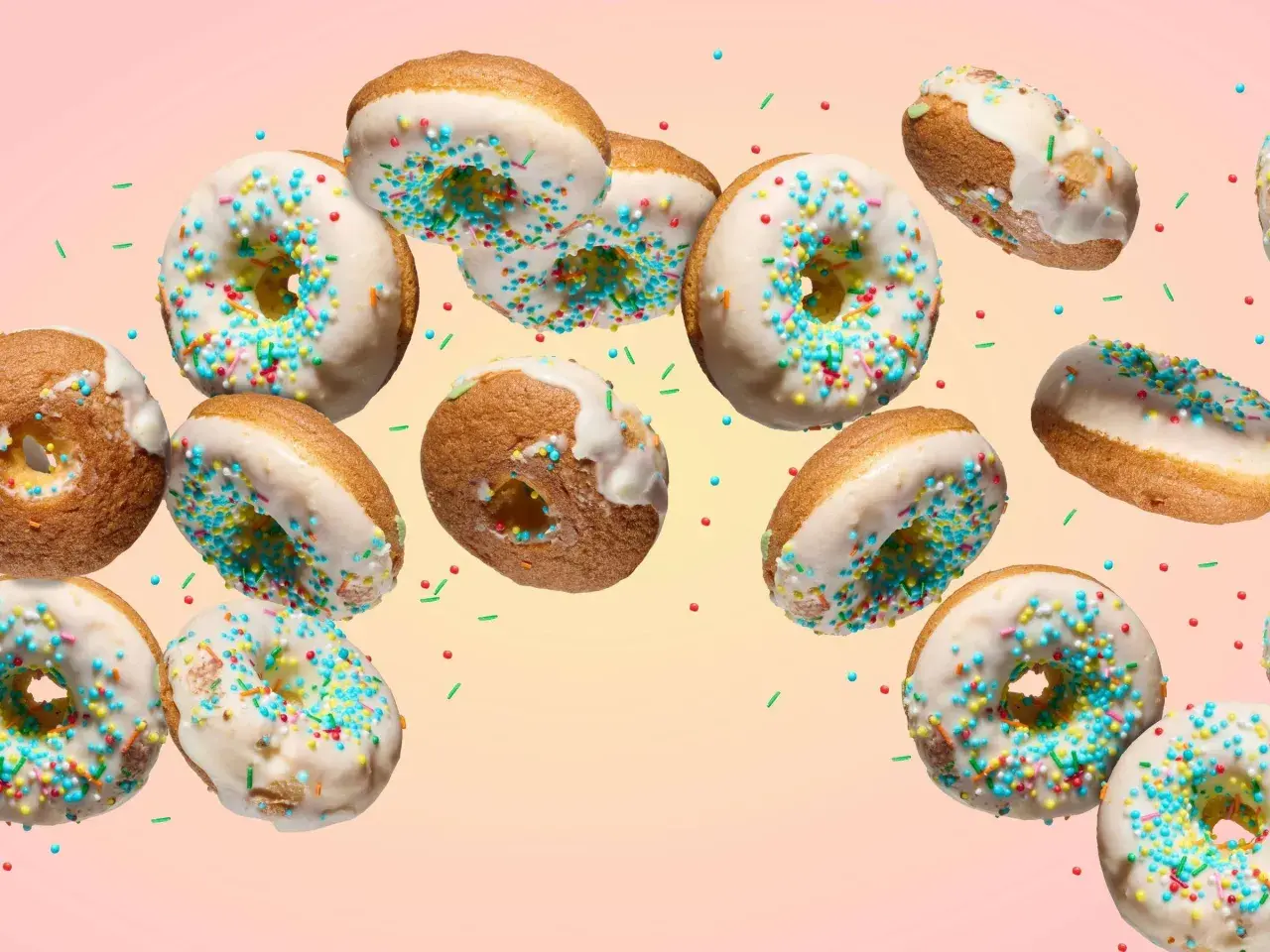 Bunte Donuts mit weißer Glasur und Streuseln schweben im Bild. Ein köstliches Rezept für selbstgemachte Donuts.