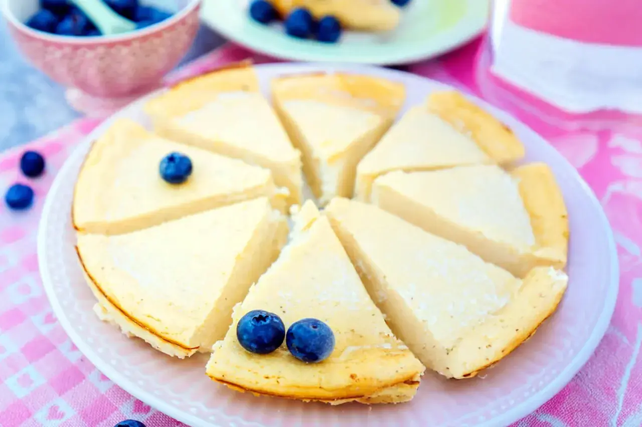 Ein cremiger, kalorienarmer Kuchen mit Blaubeeren, der auf einem rosa karierten Tuch serviert wird.