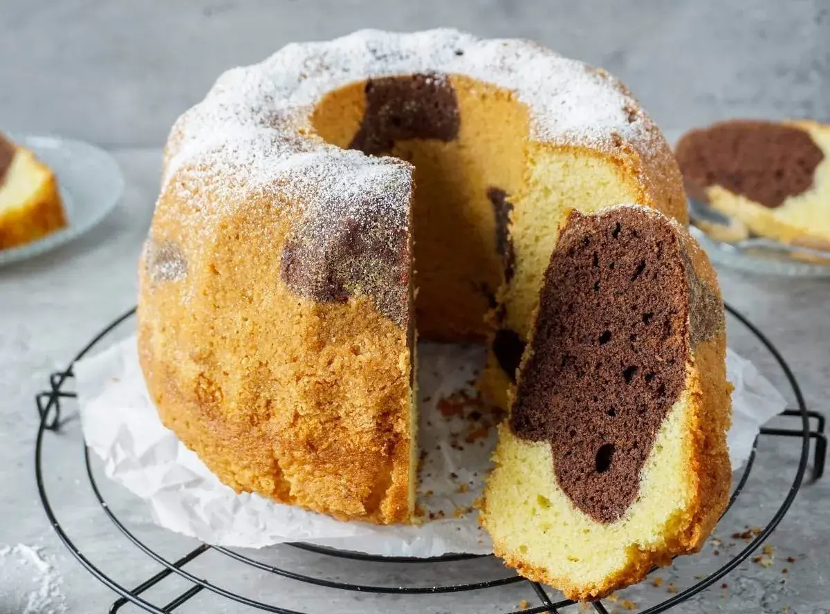 Ein saftiger Marmorkuchen, der zeigt, wie einfach backen sein kann. Mit Puderzucker bestäubt und einem Stück herausgeschnitten.