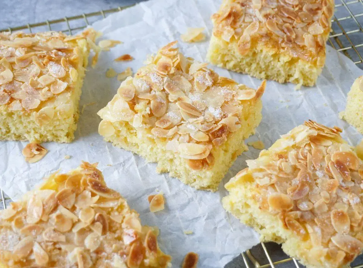 Saftiger Buttermilch Kuchen mit knusprigen Mandelblättchen und Zucker bestreut, auf Backpapier und einem Gitterrost.