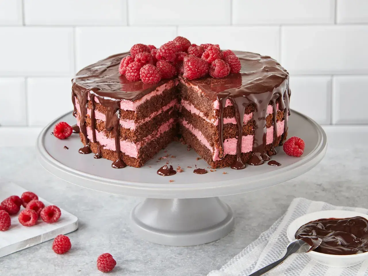 Schoko Himbeer Torte mit drei Schichten dunklem Kuchen und rosa Himbeercreme, überzogen mit Schokoladenglasur und frischen Himbeeren.