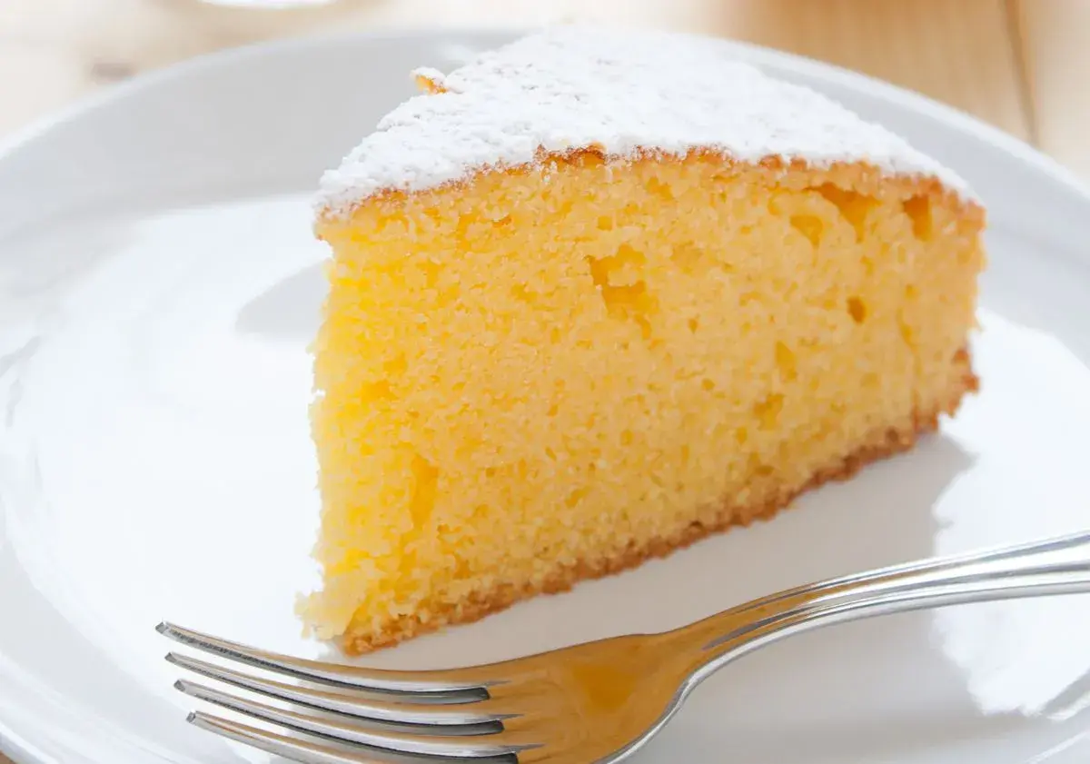 Ein saftiges Stück Vanille Kuchen, bestäubt mit Puderzucker, wartet auf dem Teller neben einer Gabel.