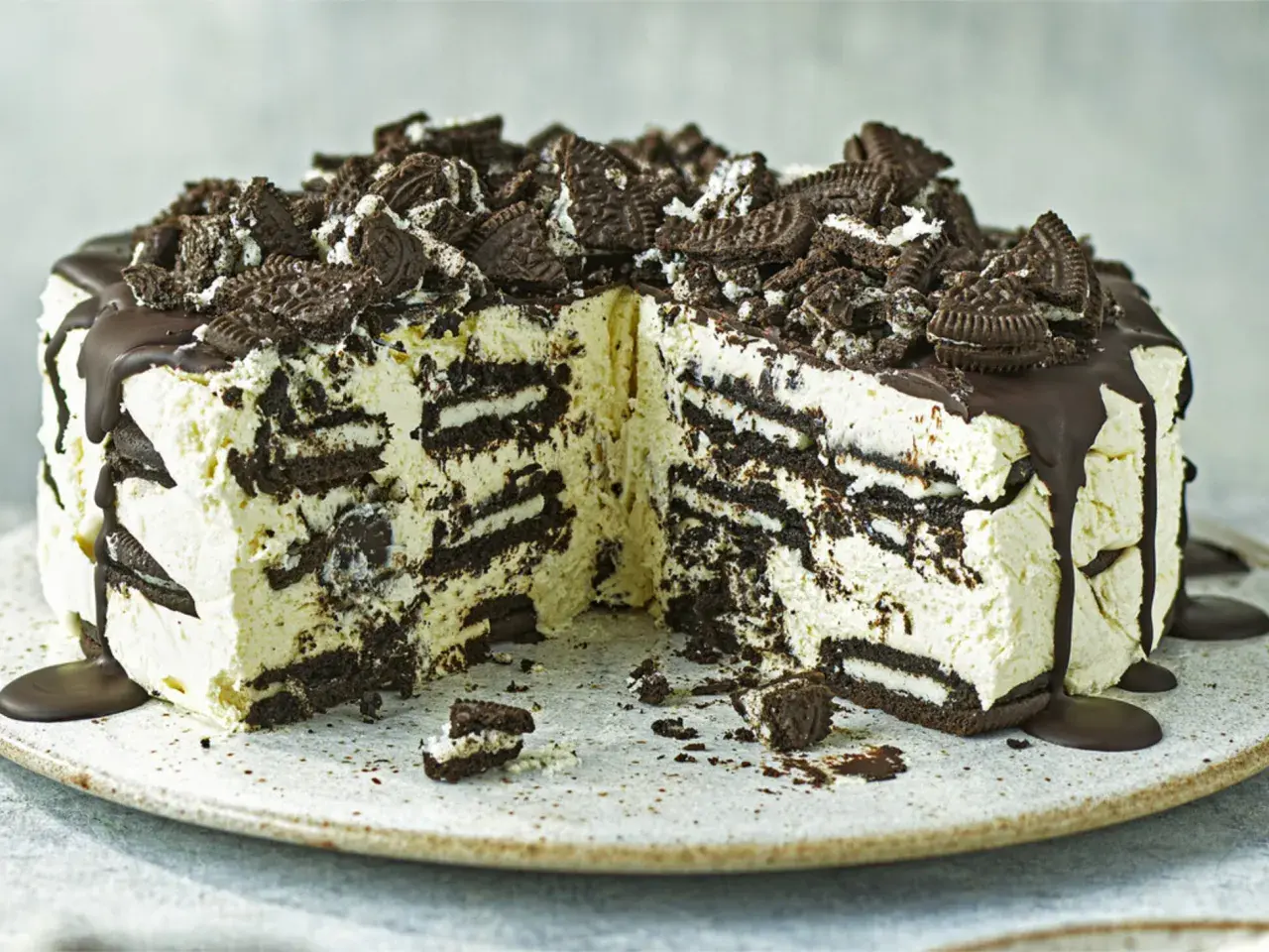 Cremige Oreo Torte mit Schokoladenguss und zerbröselten Keksen obendrauf. Ein Stück ist bereits angeschnitten.
