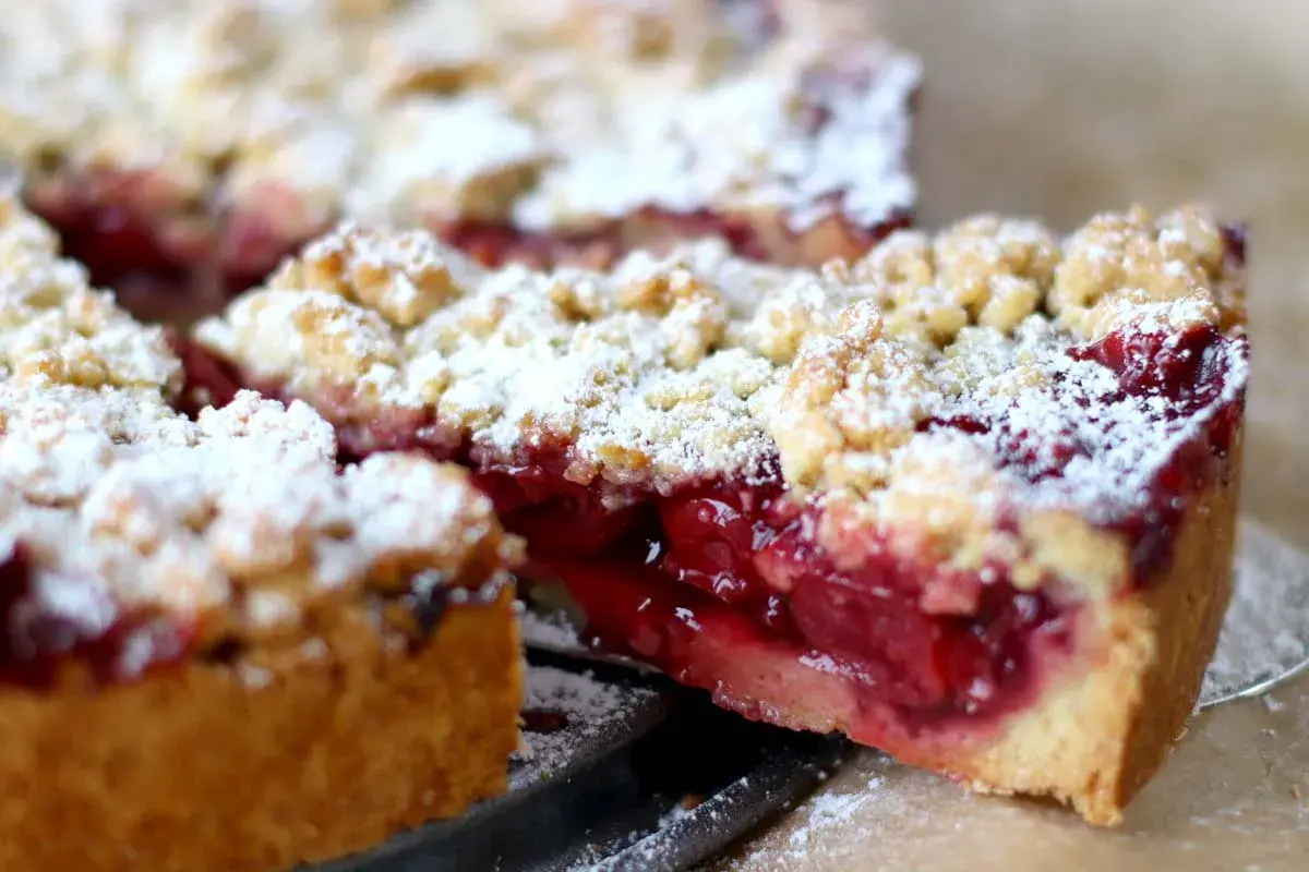 Saftiger kirschkuchen mit streusel, bestäubt mit Puderzucker. Ein Stück wurde herausgeschnitten, um die roten Kirschen zu enthüllen.