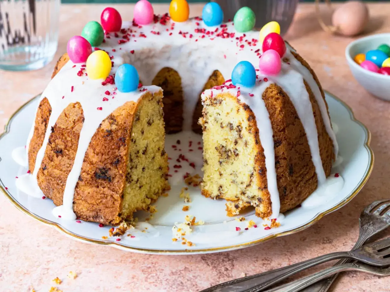 Ein Gugelhupf mit Schokoladenstückchen, Zuckerguss und bunten Ostereiern. Dieses Gugelhupf Rezept ist perfekt für Ostern.