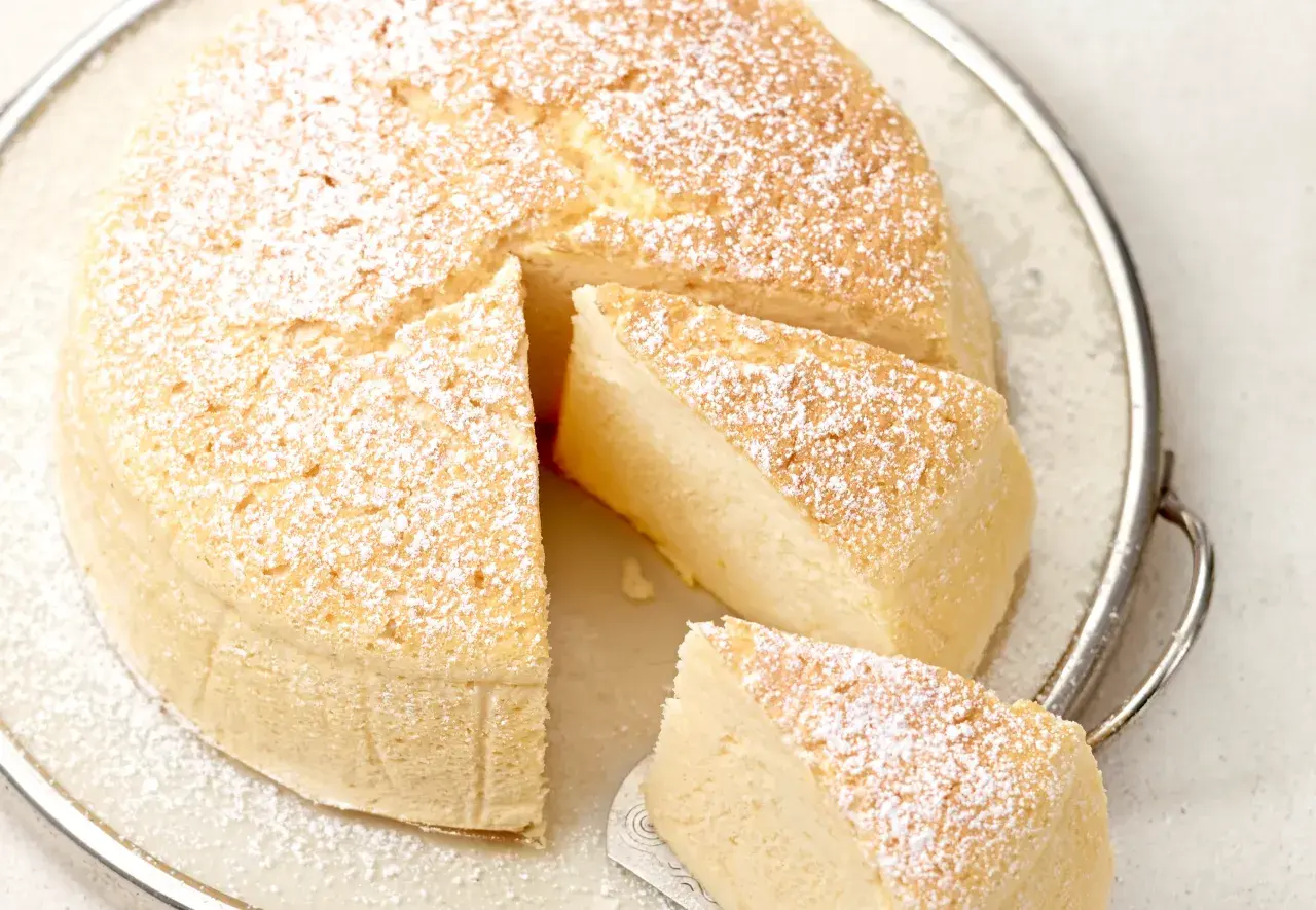 Ein luftiger, fluffiger japanischer Cheesecake, bestäubt mit Puderzucker, auf einer Servierplatte.