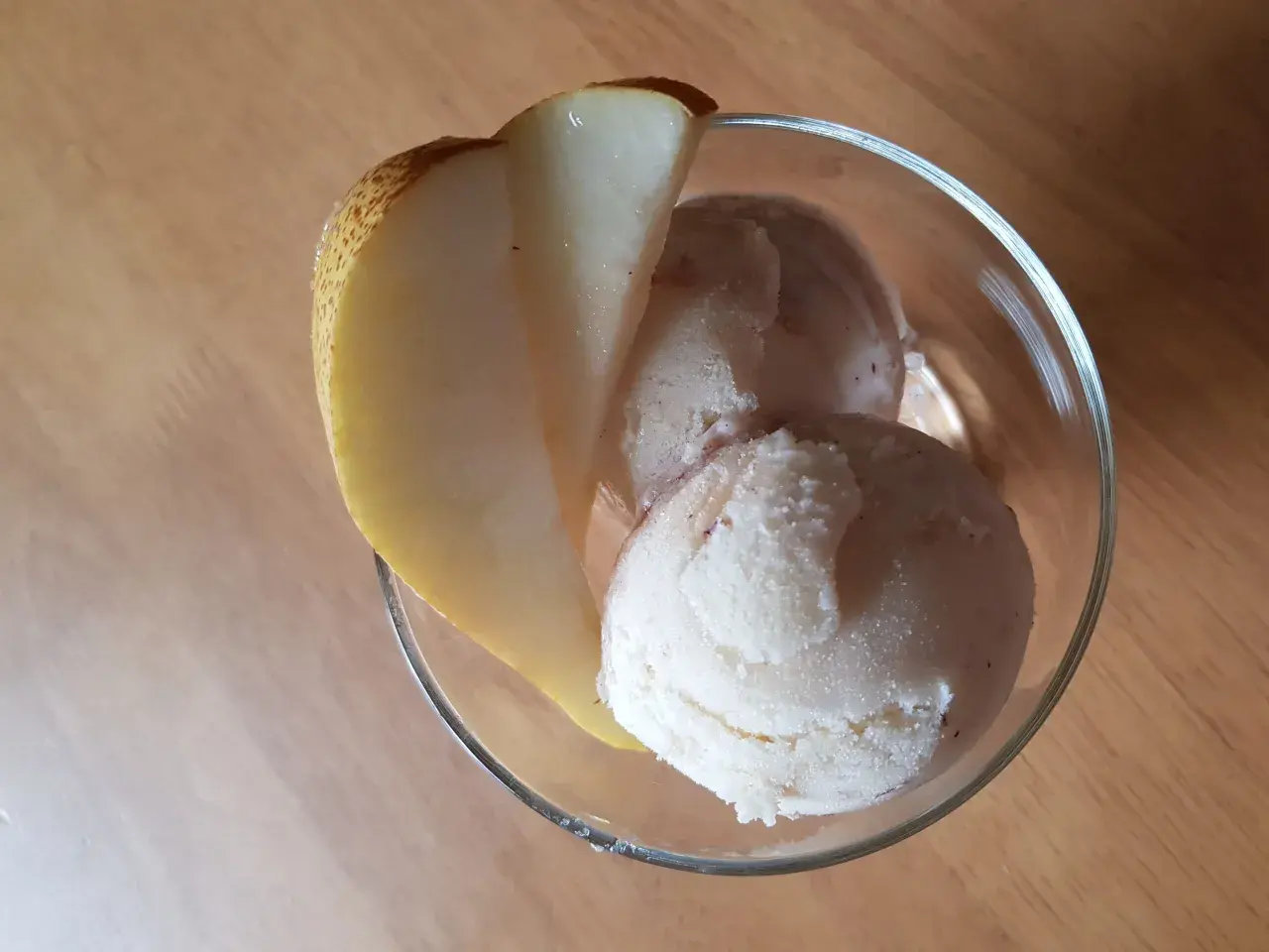 Ein Glas mit cremigem birnen eis, garniert mit einer frischen Birnenspalte, steht auf einem Holztisch.