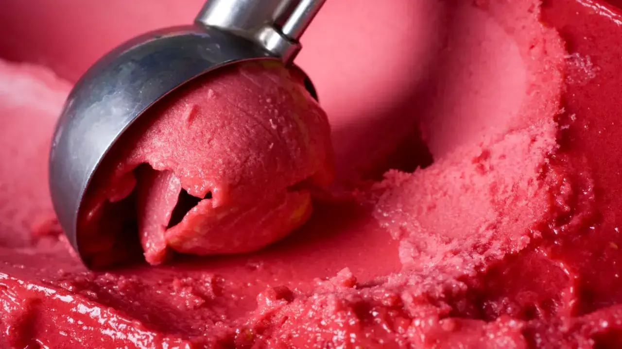 Ein Löffel nimmt eine Kugel leuchtend rotes Eis auf. Es sieht aus wie ein köstliches Eis mit Ei, das auf der Zunge zergeht.